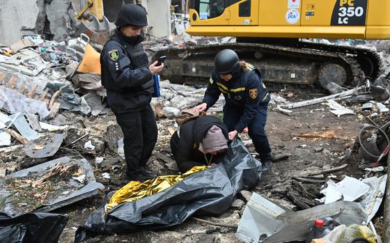 A grieving Ukrainian mother comforted by law enforcement surrounded by the debris of a damaged building.