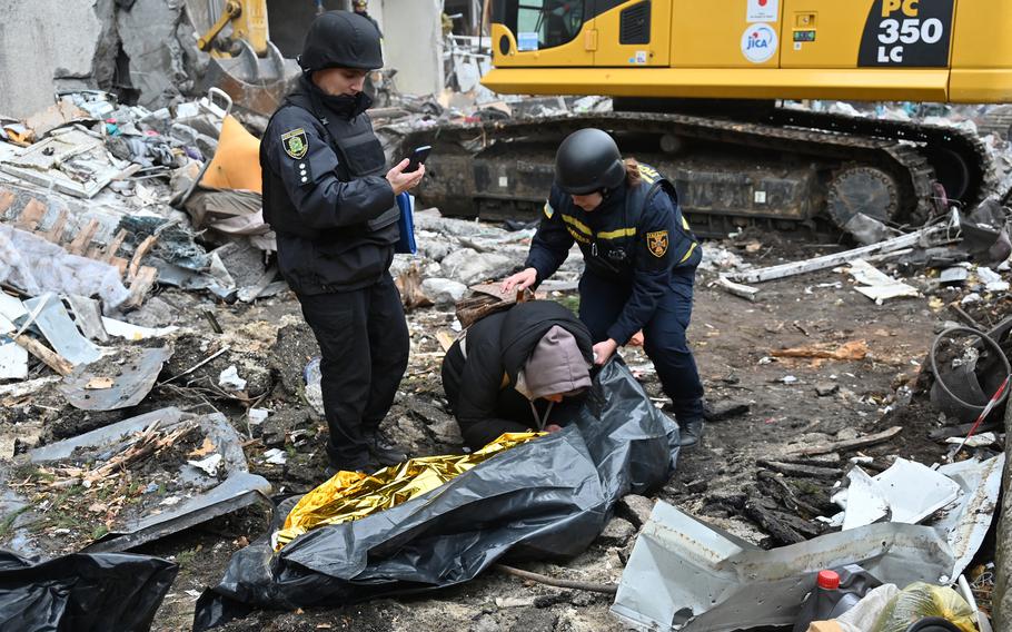 A grieving Ukrainian mother comforted by law enforcement surrounded by the debris of a damaged building.