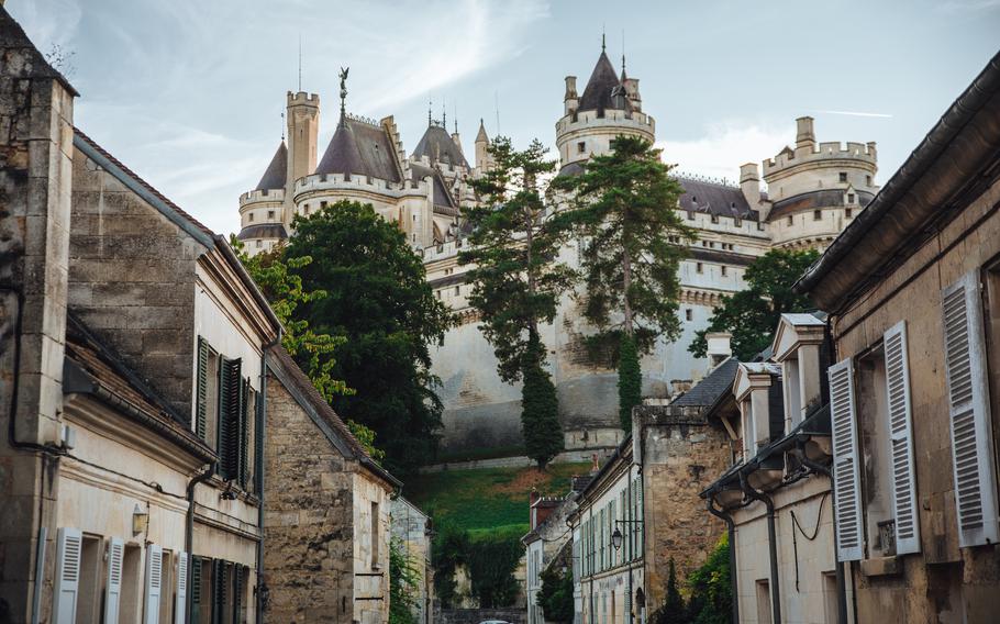 Pierrefonds castle and trees rise up at the end of a street with brick and stone houses in France.