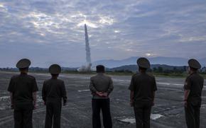 North Korean leader Kim Jong Un stands in the center of five men who are watching a missile launch. 