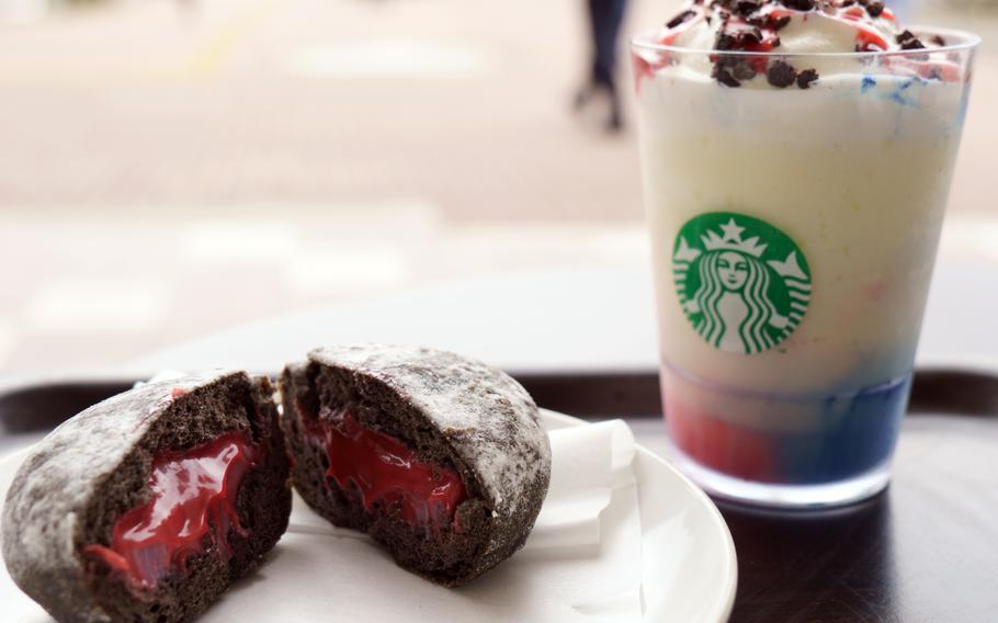 A fluffy brown pastry cut open to expose red filling and a colorful drink with a cup with a Starbucks logo sit on a table.