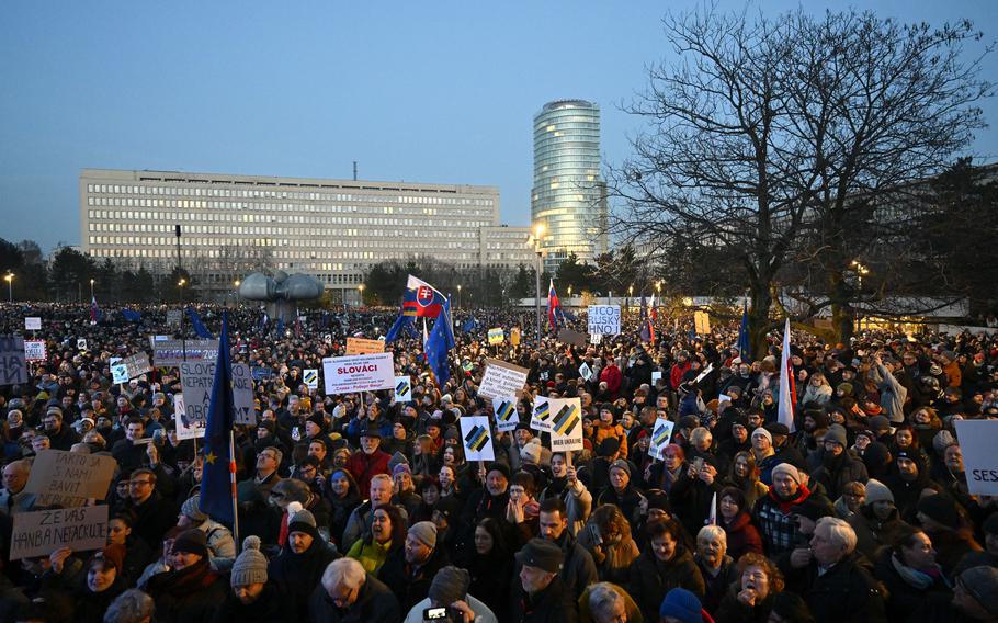 A mass of people is seen from a higher angle with buildings in the background.