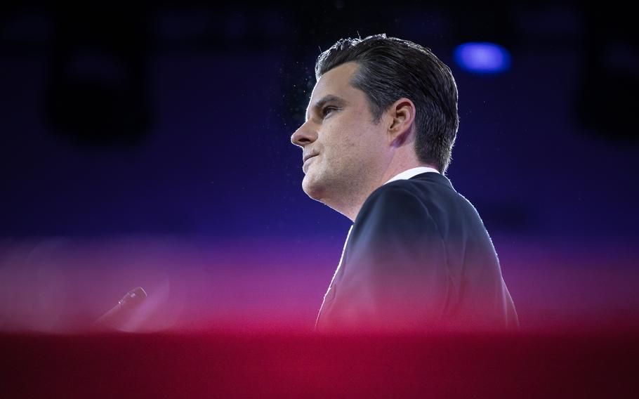 A man wearing a suit speaks into a microphone in a darkened auditorium.