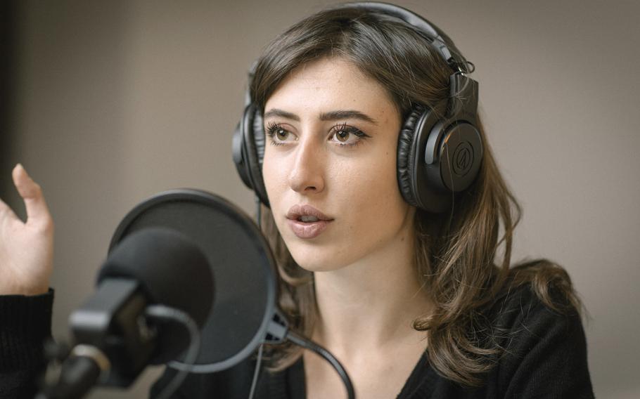 A woman with headphones on is seen from the shoulders up, speaking in front of a microphone.