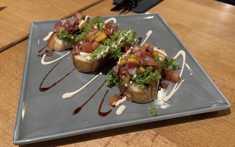 Bruschetta with brown and white swirls of sauce on a square plate.