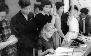 Kadena, Okinawa, March 21, 1958:  Miss Haruko Ota, a third grade teacher, peeks over the shoulder of Brenda Sheets, 10, daughter of Master Sgt. and Mrs. W. G. Sheets, as pupils with the right answer raise their hands in their Kadena Air Base fourth grade classroom. Around them a group of Okinawan teachers and parents look over the shoulders of the pupils. Forty-nine Okinawan educators got a first-hand look at American educational methods and were surprised that American students "feel so much at ease in school." The group toured the Kadena Air Base Dependent Elementary School in a visit sponsored by the Ryukyuan-American Community Relations Committee.

The exchange of educational knowledge between US and Okinawan teachers has continued to this day as this recent article testifies. https://www.stripes.com/theaters/asia_pacific/2024-11-07/dodea-schools-coteaching-okinawa-15767493.html

To read what Okinawan and American educators learned from each other back in 1958, check out the original article here. 

META TAGS: DoDEA; DODDS; school; education; dependents; Ryukyu; American-Japanese relations; international relations; Okinawans