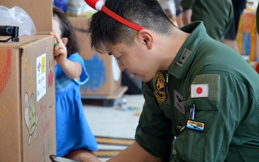 A Japanese airman wearing a red Christmas hat checks boxed during Operation Christmas Drop preparations.