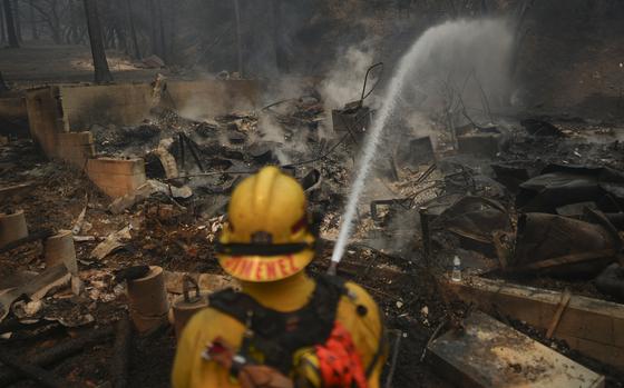 A firefighter hoses down hot spots on a fire-ravaged property while battling the Bridge Fire Wednesday, Sept. 11, 2024, in Wrightwood, Calif. (AP Photo/Eric Thayer)