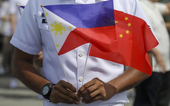 FILE - A member of the Philippine Coast Guard holds flags during the arrival of Chinese naval training ship, Qi Jiguang, for a goodwill visit at Manila's port, Philippines, June 14, 2023. (AP Photo/Basilio Sepe, File)