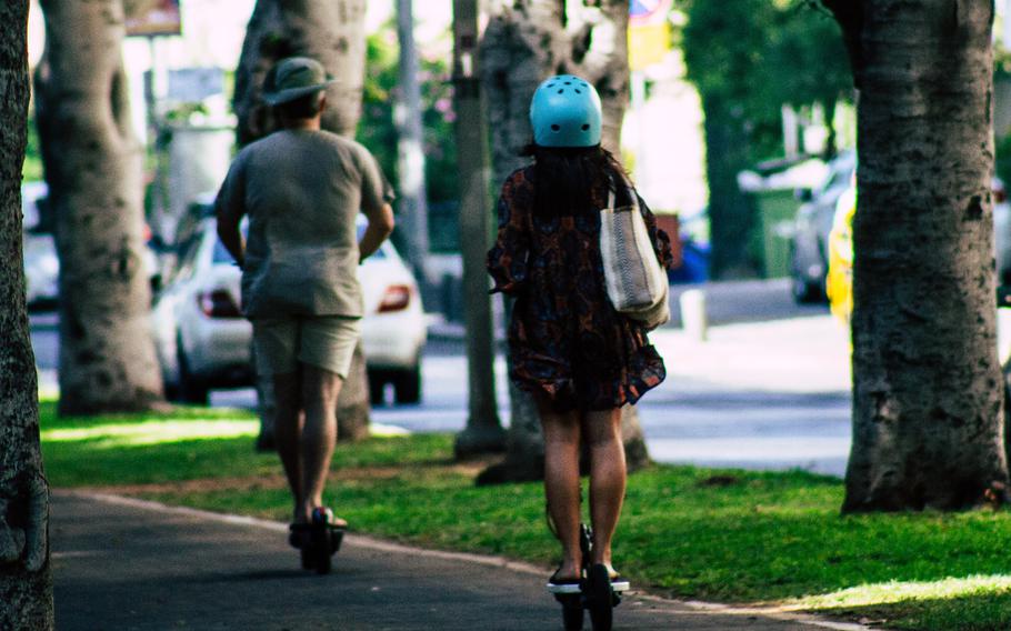 View from behind of two people riding e-scooters on a shady sidewalk