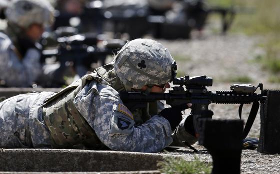 A female soldier in combat gear lies on her stomach and fires a machine gun on an outdoor firing range.