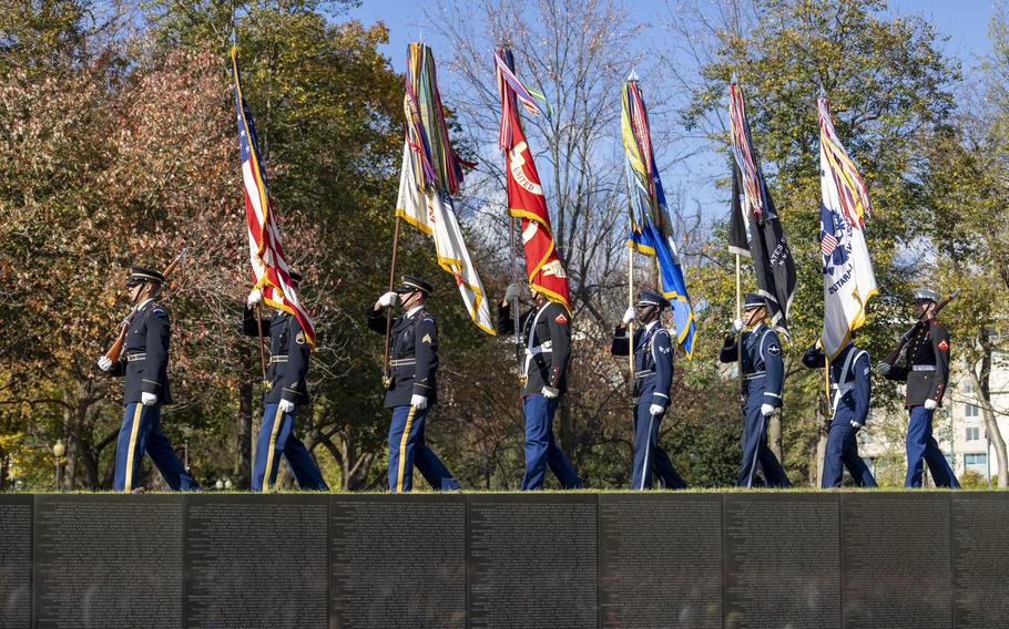 Servicee members carrying various flags march past the Vietnam Veterans Memorial.