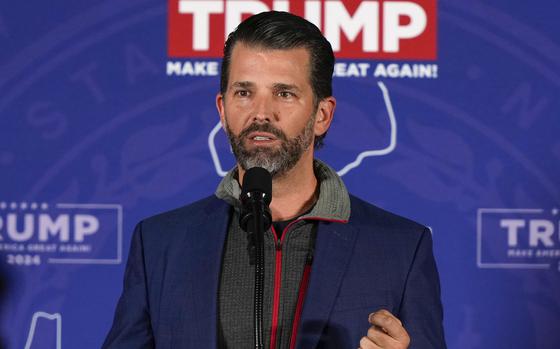 Donald Trump Jr. speaks at a microphone in front of a sign that reads “TEAM TRUMP.”