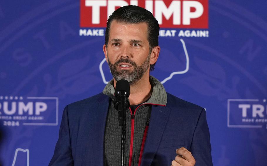 Donald Trump Jr. speaks at a microphone in front of a sign that reads “TEAM TRUMP.”