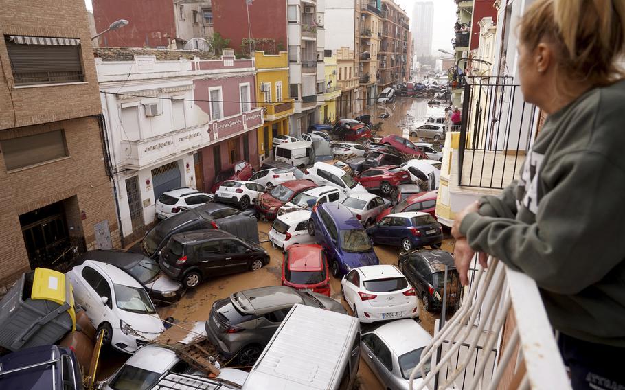 A woman looks out from her balcony at vehicles piled up and trapped on a flooded street in Valencia.