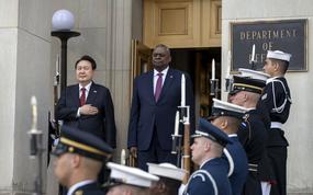 A row of military members stands in a line outside of the Department of Defense building while the defense secretary and the South Korean president stand beside one another.