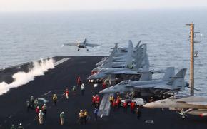 A fighter jet with smoke behind it takes off from a carrier.