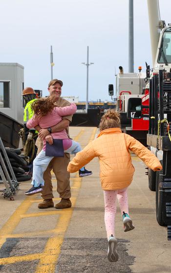 A sailor embraces his daughters as they run up to him