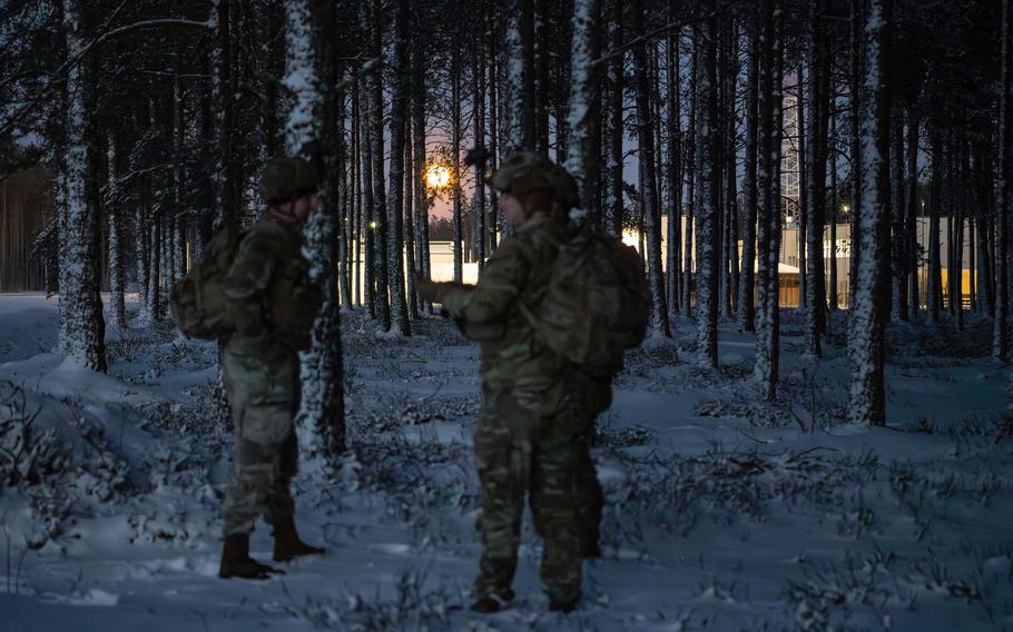 Soldiers in the snowy woods with the moon between the trees in the background.