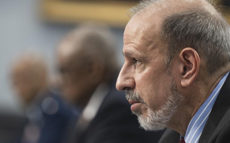 Close-up view of a bearded man in a dark suit testifying at a congressional hearing.