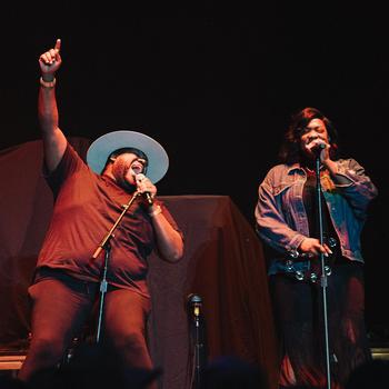 Michael Trotter raises his arm and index finger to the sky while singing with wife and bandmate Tanya Trotter.