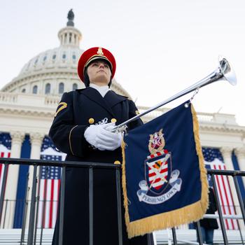 A soldier holds her trumpet with the flag-draped Capitol in the background.