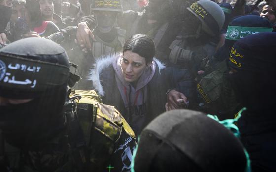 An Israeli woman hunches over while surrounded by masked militants as she is released from captivity.