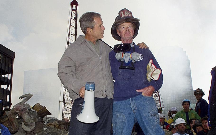 President Bush, holding a megaphone, puts his arm around Bob Beckwith, who is wearing a firefighter helmet.