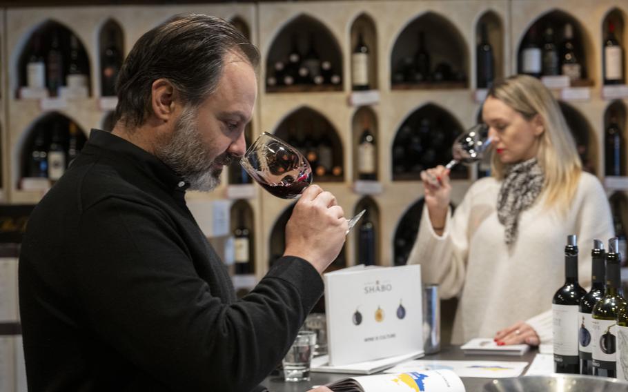 A man and a woman both hold up glasses of red wine to do a sniff test at a wine tasting.