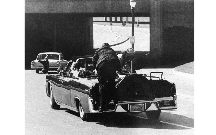 President John F. Kennedy slumps down in the back seat of the presidential limousine as it speeds along Elm Street toward the Stemmons Freeway