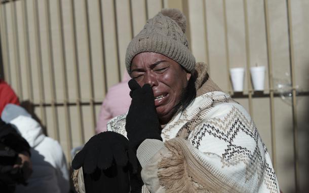 A woman wearing a hat and blanket wipes tears from her face.