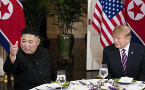 North Korean leader Kim Jong Un points at something out of the frame as he sits at a round table with Donald Trump.