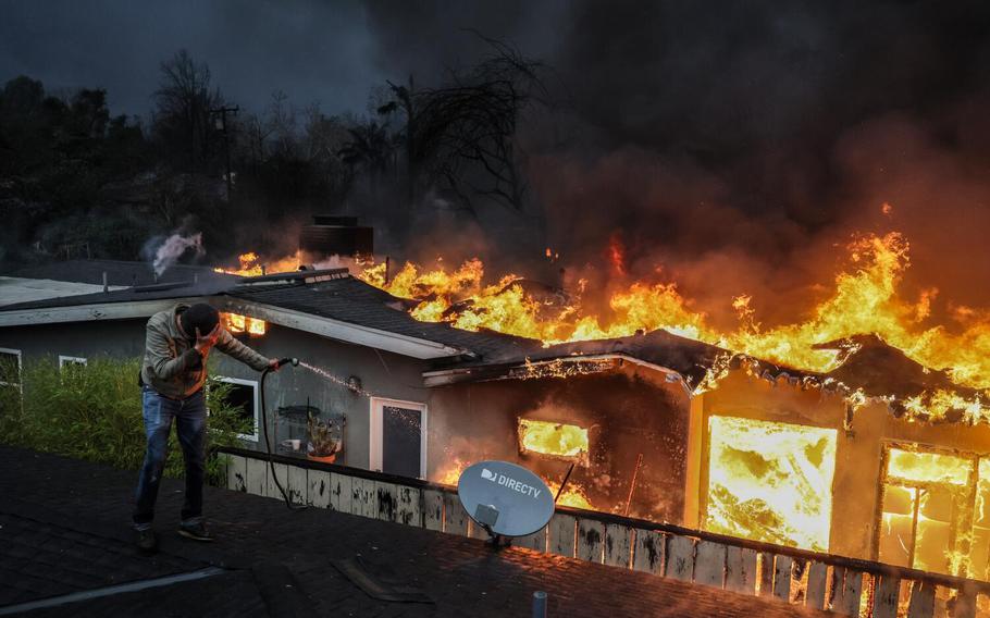 Steve Salinas shields from intense heat as he hoses down a neighbors rooftop on Sinaloa Ave. as the Eaton Fire continues to grow on Wednesday, Jan. 8, 2025, in Altadena, California. 