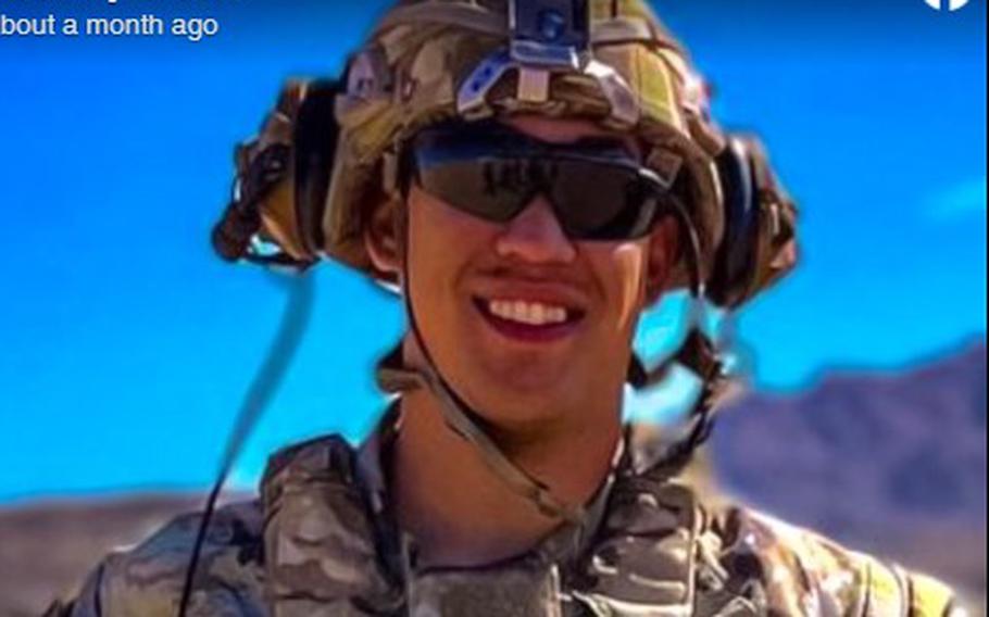 An Army soldier in combat gear and helmet stands in desert terrain with a mountain in the background.