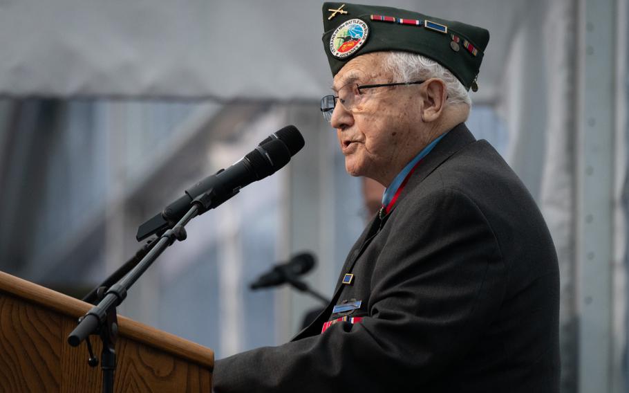 An American WWII veteran stands in uniform in front of a microphone at a podium.