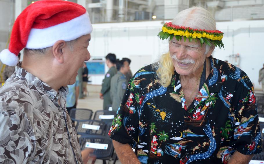 Susumu Ueda wears a Santa hat as he greets Bruce Best, who is wearing a flower crown at Andersen Air Force Base. 