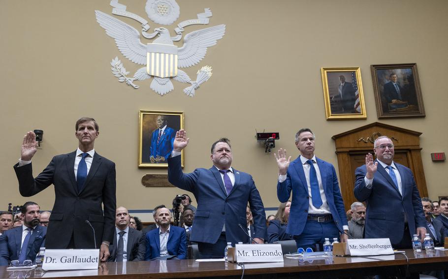 Four men in suits each hold up their right hands as they are sworn in at a hearing about UFOs.