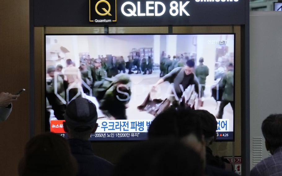 People watch a television screen with blurry video of possible North Korean soldiers collecting boxes.