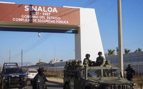 A sign indicates Mexico’s Sinaloa state as military and police patrol the area.