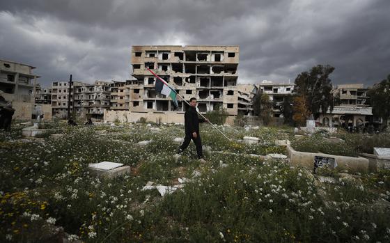 FILE - A man carries Palestinian flag in a Palestinian refugee camp of Yarmouk in Damascus, Syria, Monday, March 20, 2023. At least seven people have been arrested in Germany and Sweden on suspicion of allegedly having committed crimes against humanity and war crimes in Syria in 2012-2014, authorities in the two countries said Wednesday, Wednesday, July 3, 2024. (AP Photo/Omar Sanadiki, File)