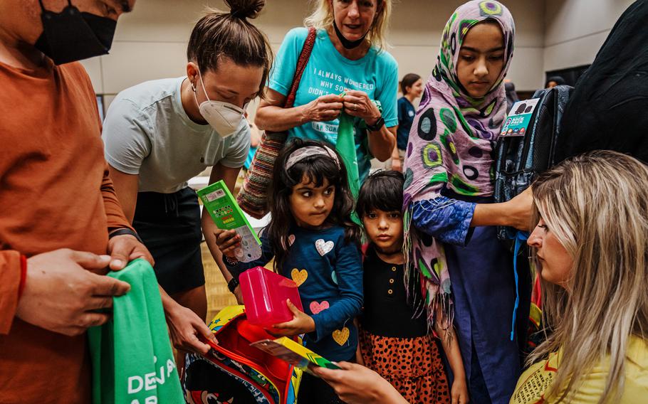 Rahmat Gul Safi, left, looks on as children, from left, Bus Bibi, 4, Zinab Safi, 3, and Shabo Gul, 8, collect free back-to-school supplies from members of Des Moines Refugee Support, who are helping newly arrived Afghan refugees in Iowa, on Aug. 6, 2022. 