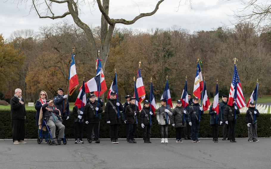 Veteran Ceo Bauer sits to the left of a line of adults and children standing for the U.S. national anthem.