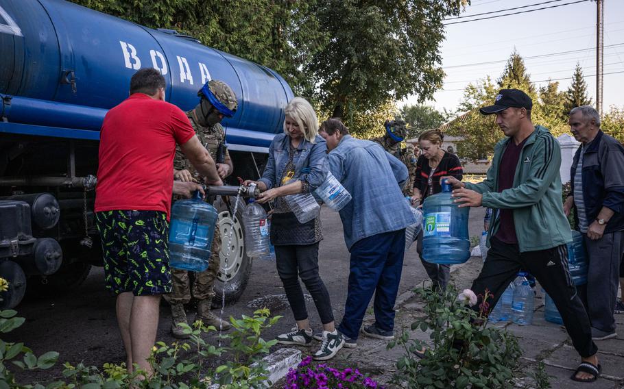 Russians fill up water bottles from a tank manned by Ukrainian soldiers in Sudzha.