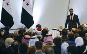 Syria’s interim president standing on the right before rows of seated people.