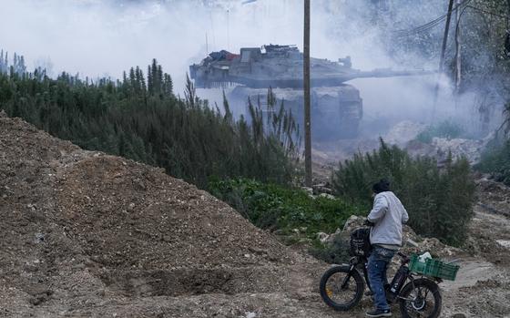 A tank emerges from the smoke in front of a man on a bicycle.