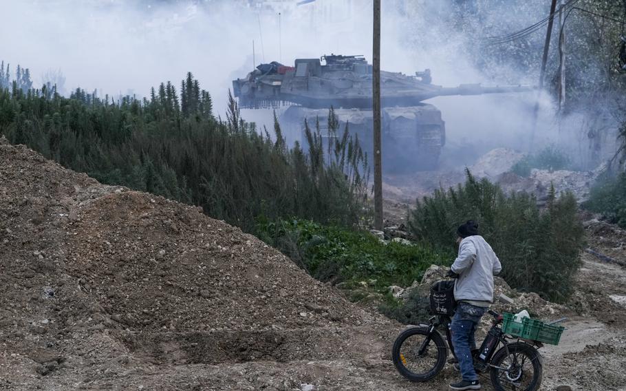 A tank emerges from the smoke in front of a man on a bicycle.