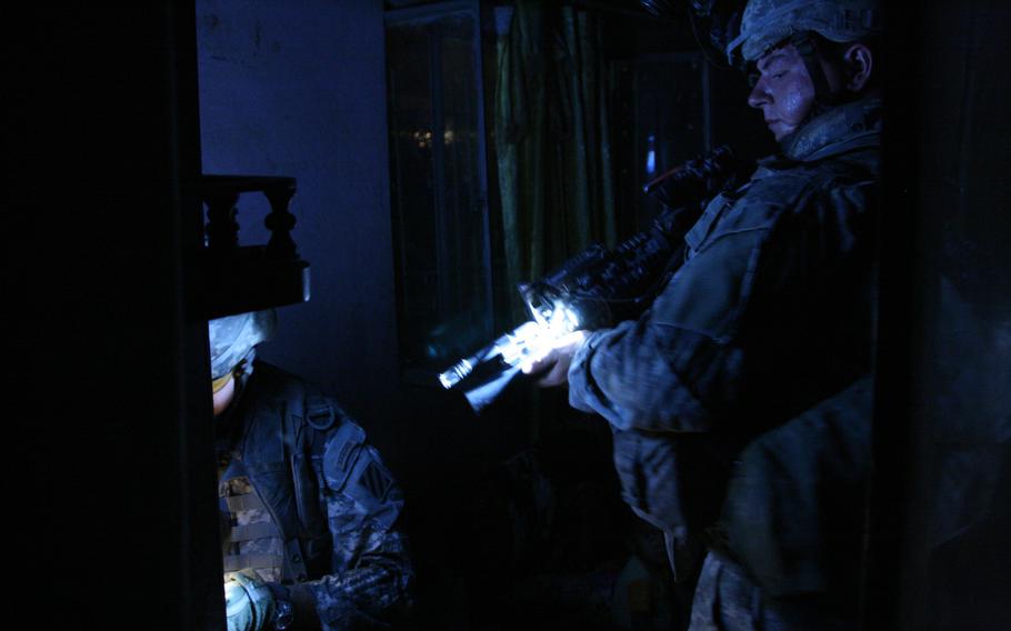 Arab Jabour district, Iraq, Jul. 5, 2007: Pvt. Erik Stroehlein, 22, of Bennington, Vt., holds a light for Capt. Eric Melloh, 30, of Huntsville, Texas, during the search of the home of a man suspected of helping insurgents direct mortar fire at Forward Operating Base Murray in Iraq’s Arab Jabour district southeast of Baghdad. Both men are from Company A, 1-30th Infantry, 3rd Infantry Division based at FOB Murray. 