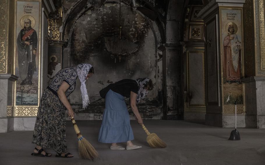 Women use straw brooms to sweep the dusty floor inside the cathedral. 