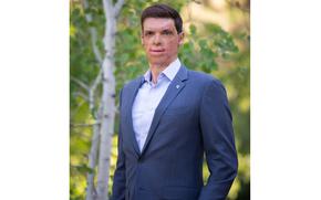 Brown poses in a suit without a tie standing next to a tree.