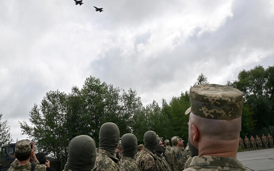 Ukrainian pilots and others look on as F-16 fighter jets fly past during a ceremony held to mark Ukrainian Air Forces Day at an undisclosed location on Aug. 4, 2024.